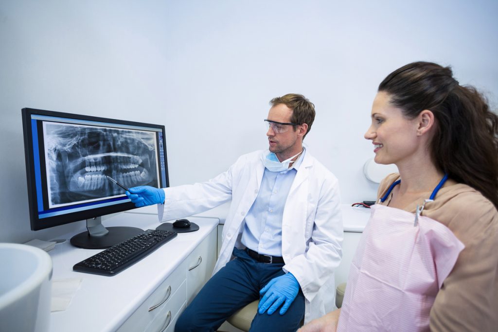Vrouw bij de tandarts krijgt röntgenfoto van kunstgebit uitgelegd
