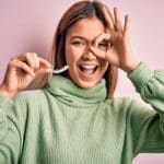 junge frau lacht haelt unsichtbare zahnschiene in der hand