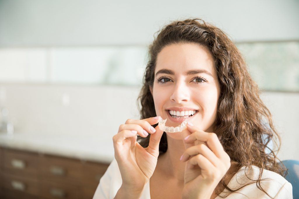Kvinna ler medan hon håller tandställningen framför munnen - Förkorta Invisaligns användningstid