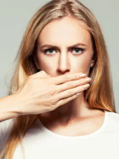 Vorderzähne schief: Junge Frau hält sich die Hand vor den Mund
