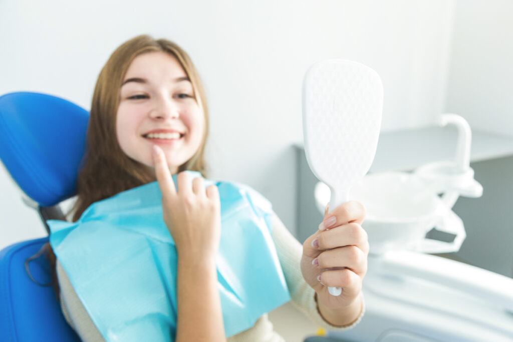 Frau hält beim Zahnarzt einen Spiegel in der Hand - schiefe Zähne bei Erwachsenen