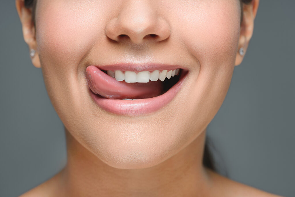 young woman licks her teeth - What is a Retainer for Teeth?