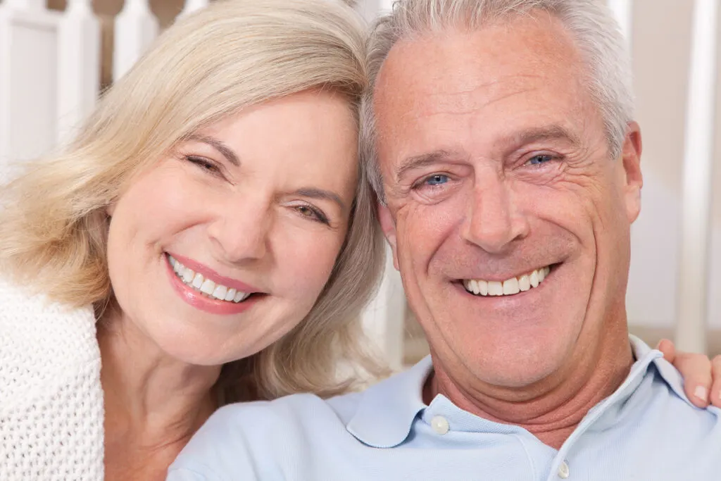 Äldre par ler mot kameran - raka tänder på ålderns höst