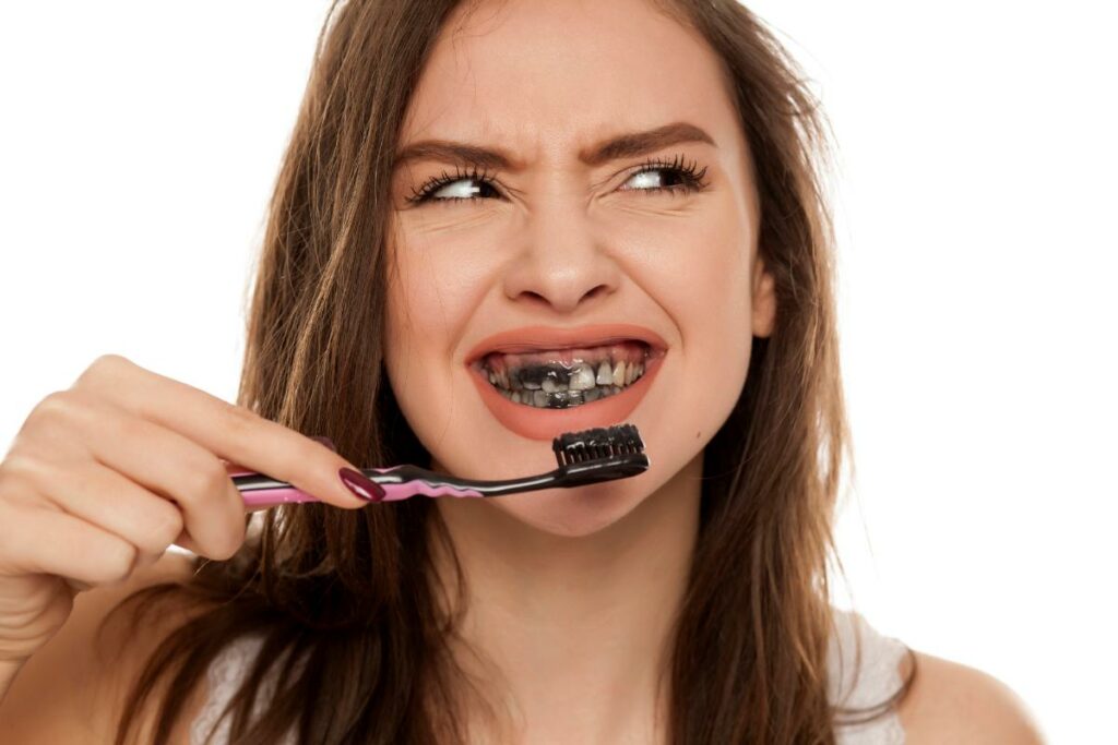 Une femme se brosse les dents avec du charbon actif - Blanchir les dents avec des remèdes maison